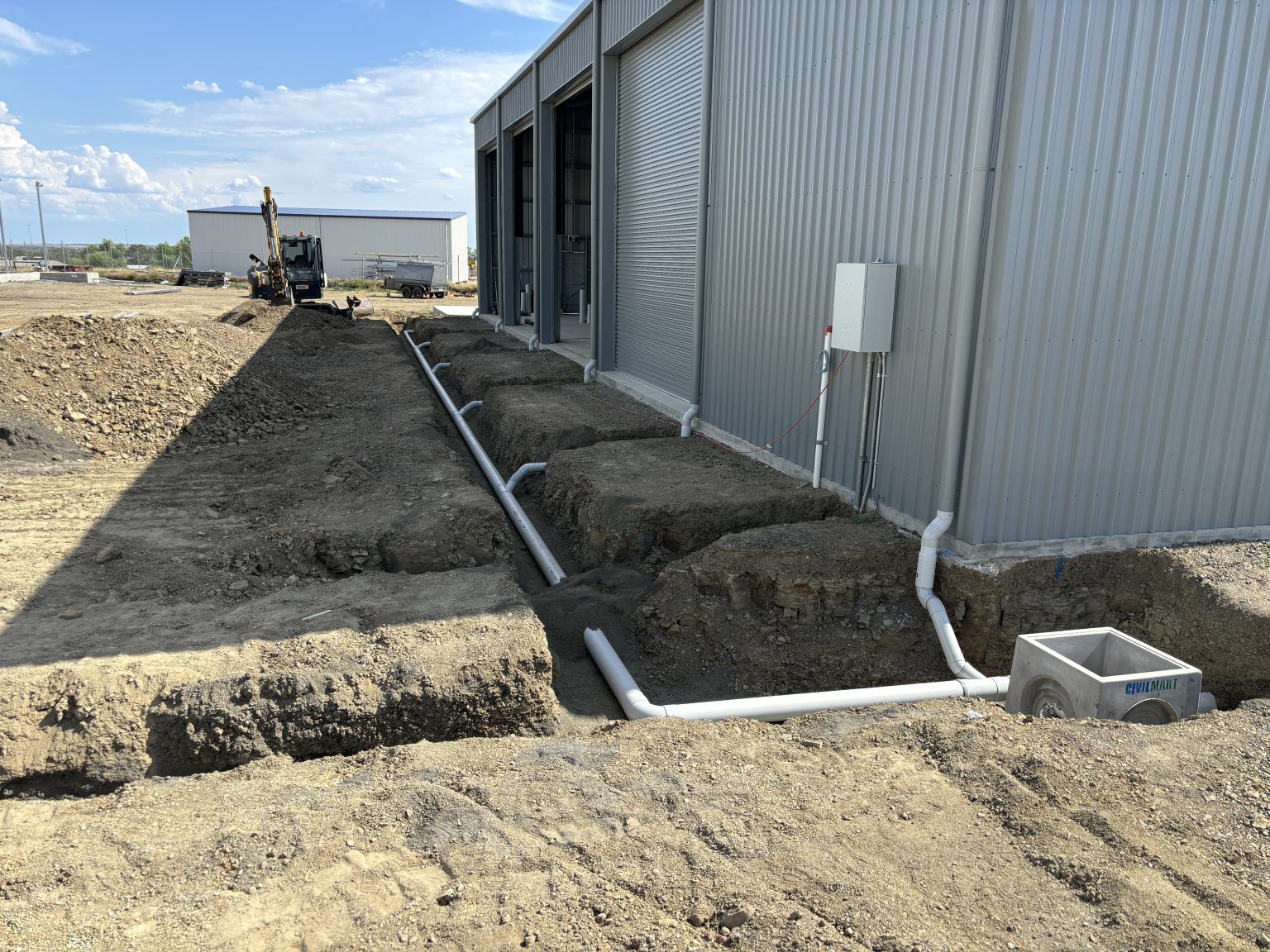 Roma Plumbing trenching and installing PVC stormwater drainage alongside a commercial building