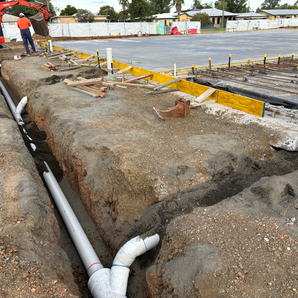 Underground PVC drainage pipes installed beside a concrete slab ahead of a building foundation